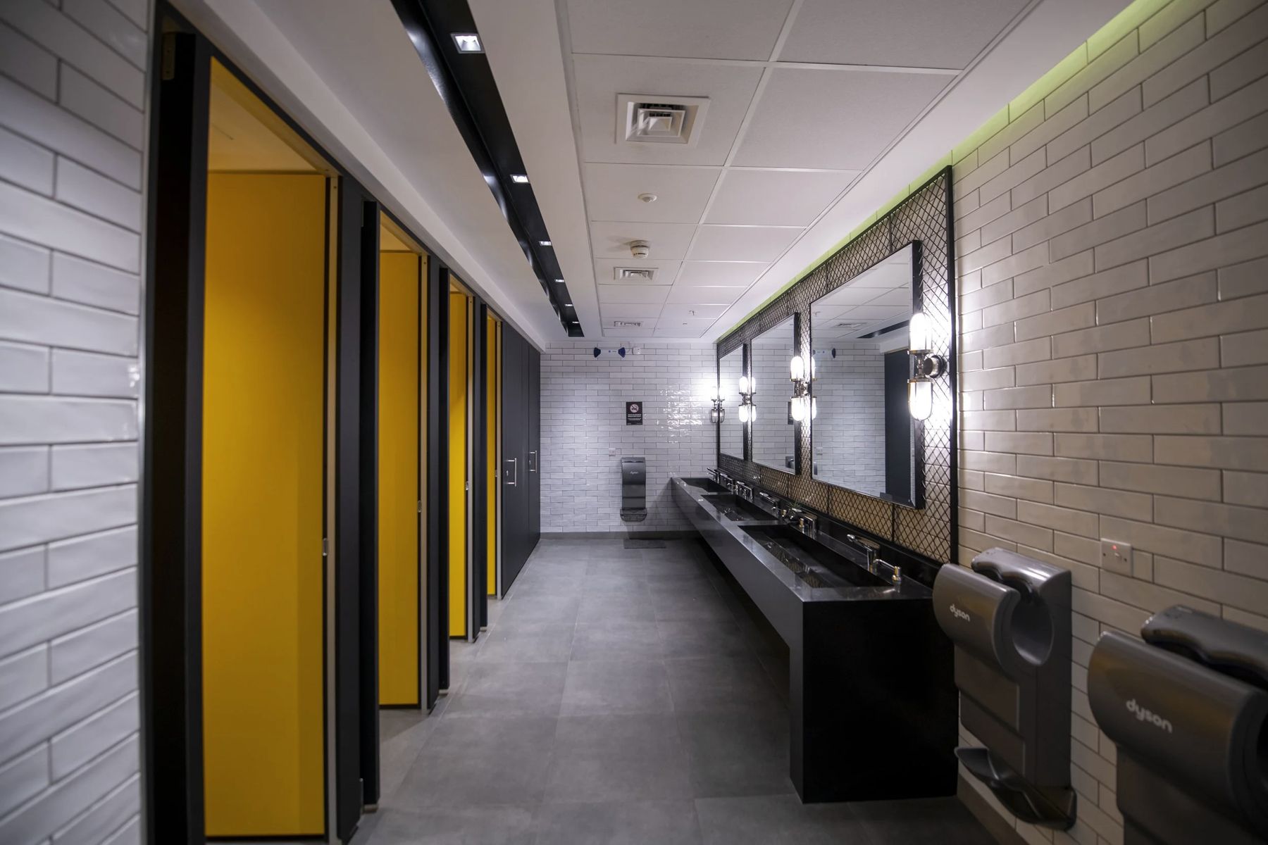 Yellow cubicle doors along a dark brick washroom corridor