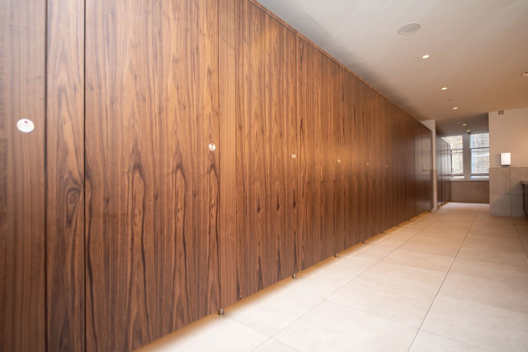 A long run of walnut-faced cubicle doors in a finished washroom