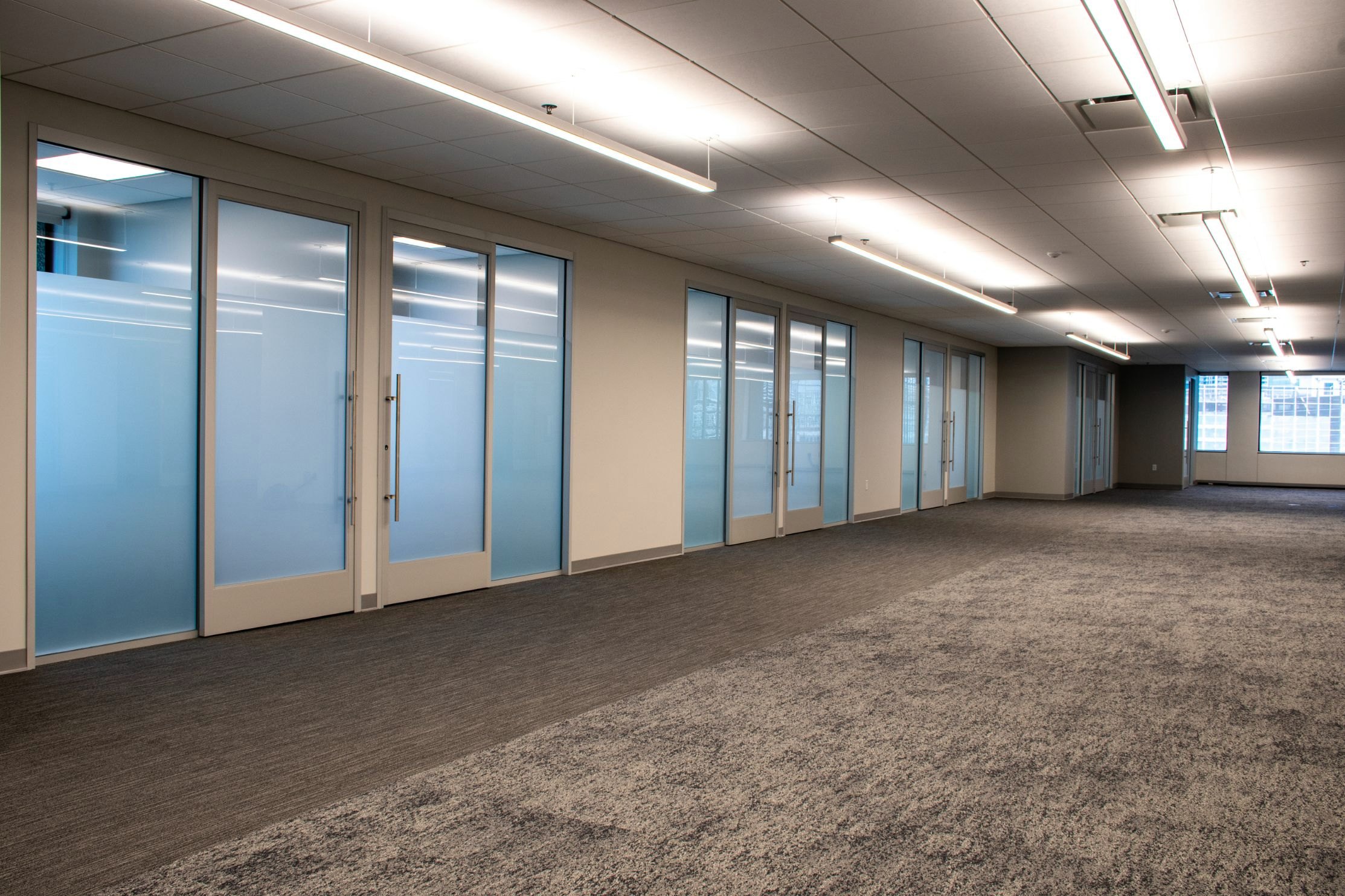Frosted glass sliding office fronts along a carpeted workplace corridor