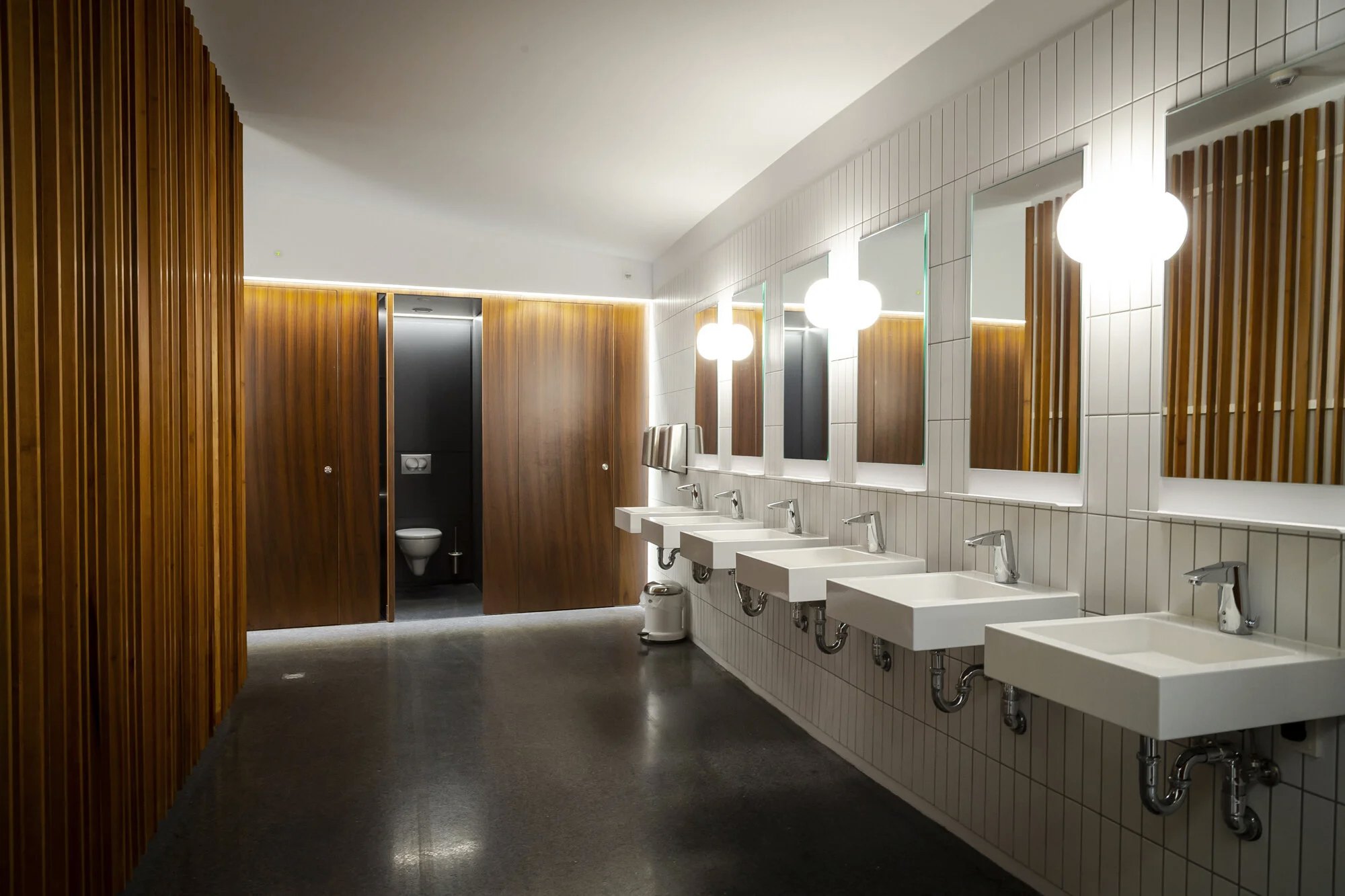 Timber cubicles and a run of wall-hung basins in a commercial washroom